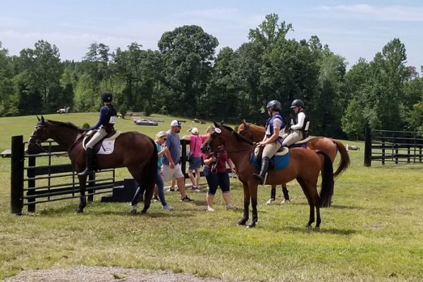 Win Green Cross country schooling facility, riders on horses standing in field.